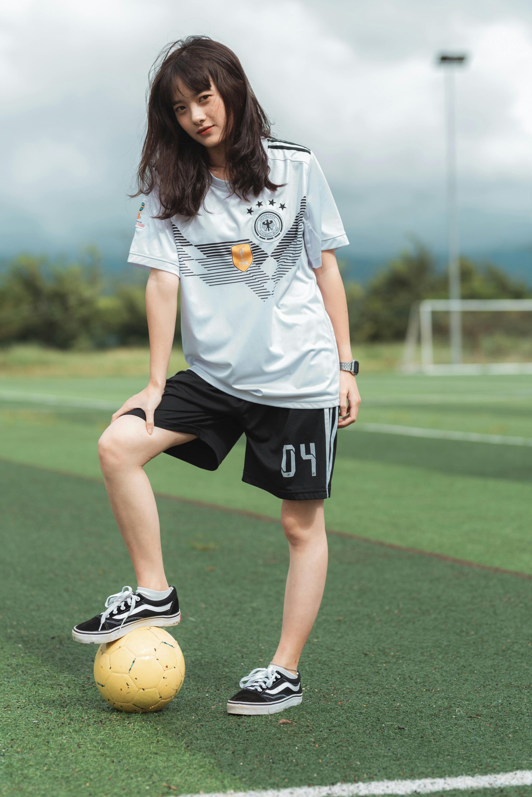 A young woman in sportswear posing with a soccer ball on a field. Perfect for sports and lifestyle themes.