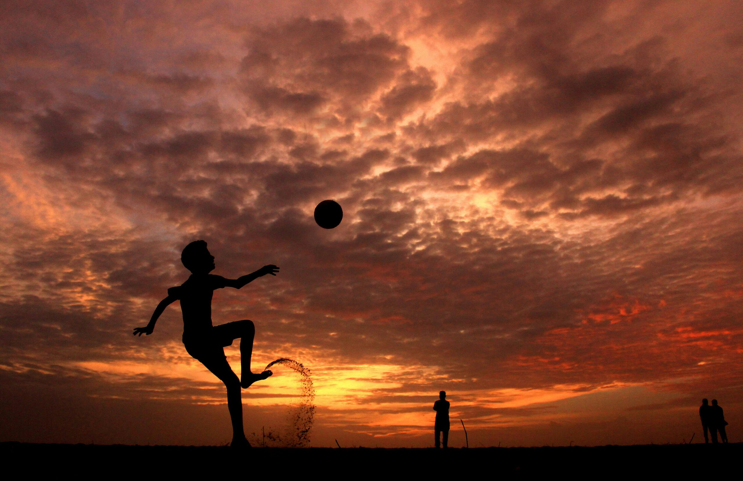 A child playing soccer on the beach at sunset in Kochi, India, creating a striking silhouette against the vibrant sky.